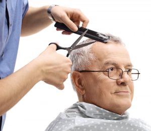 Senior man getting a haircut from a barber using scissors and and a comb.