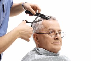 Senior man getting a haircut from a barber using scissors and and a comb.